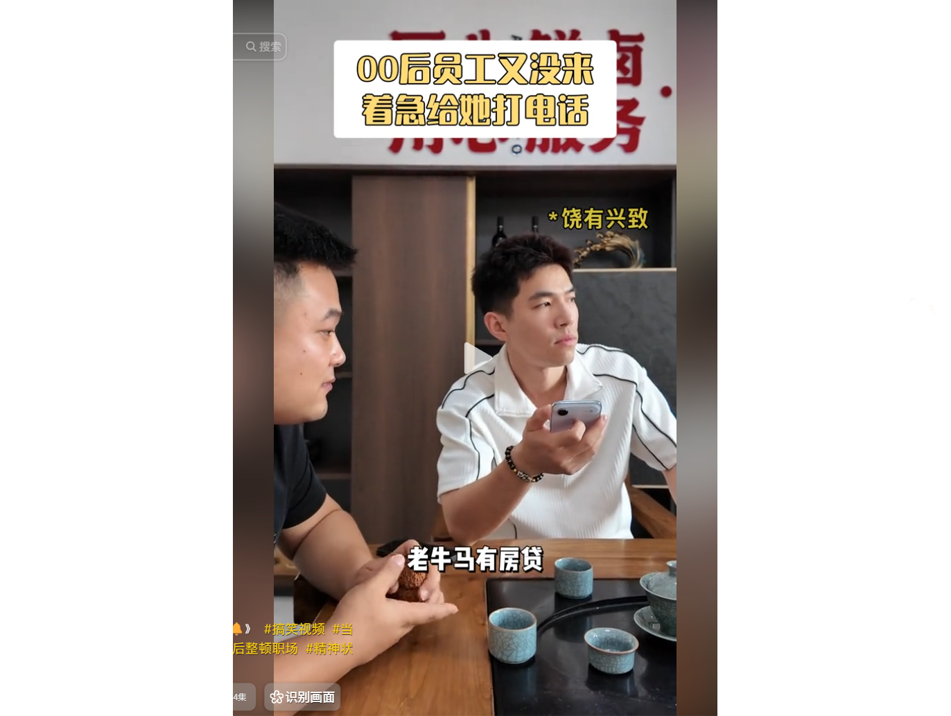 Two men sit at a table with tea cups, one holding 
