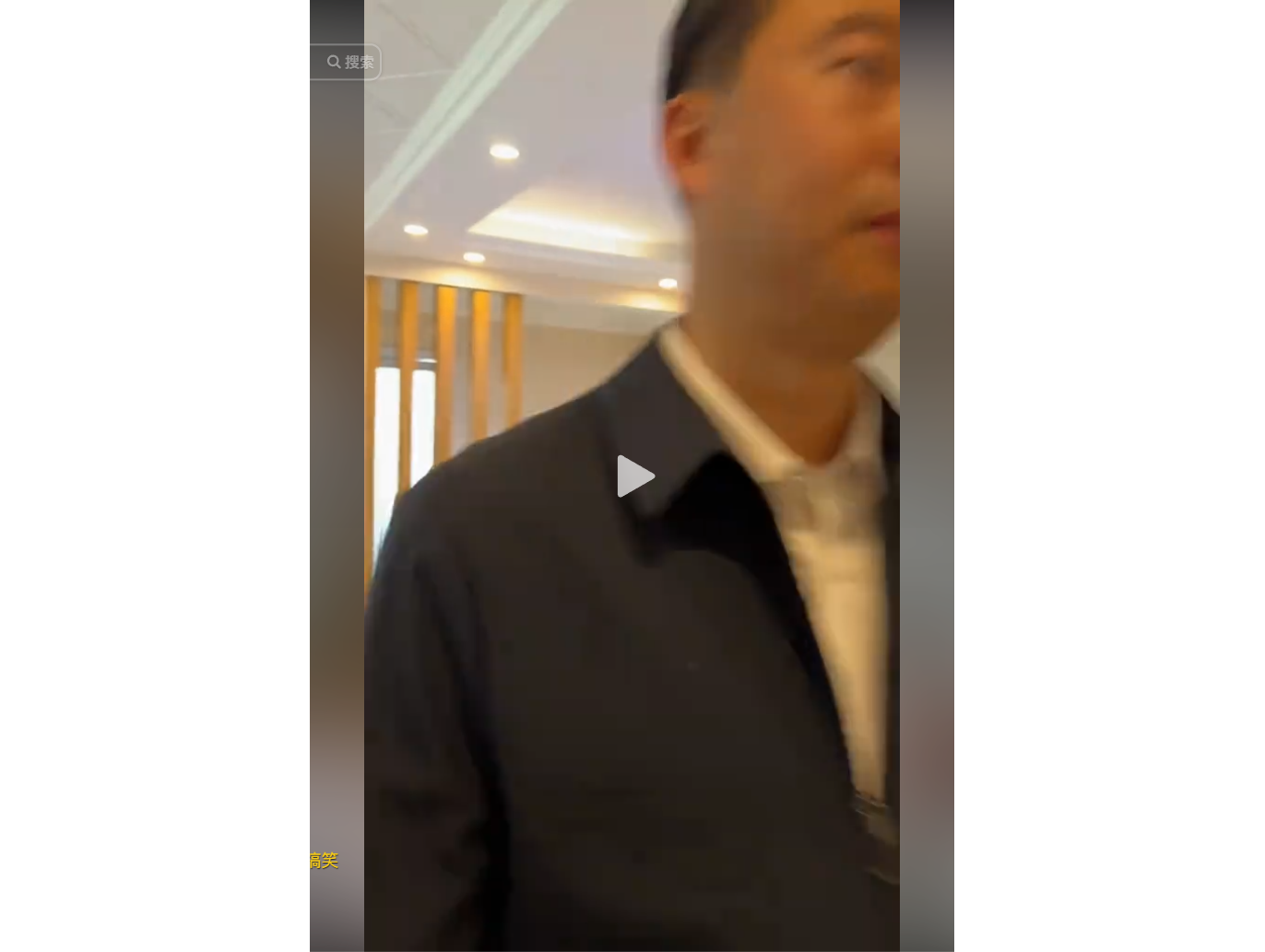 A man in a dark suit and white shirt stands indoor