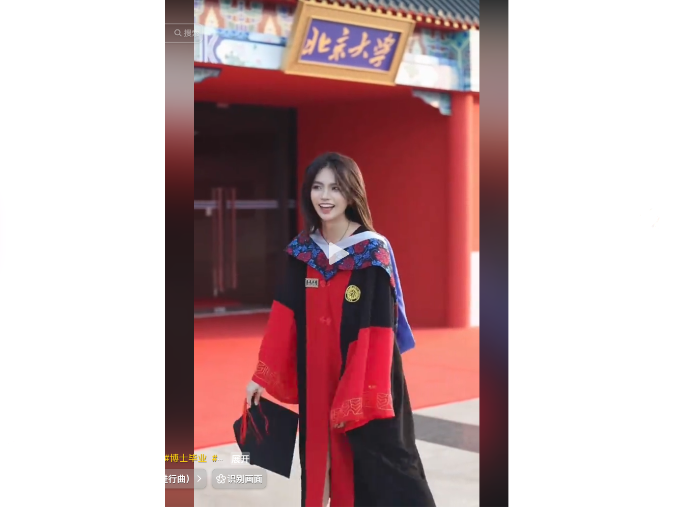 A graduate in a red and black academic gown smiles